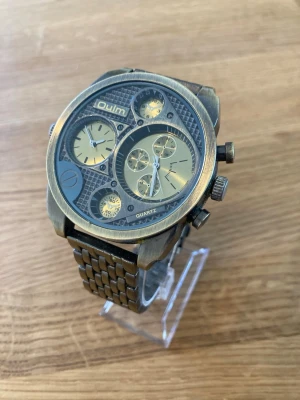 Oulm Chrono Dual Time 50mm Herrklocka - Säljer en Oulm Chrono Dual Time herrklocka. Klockan är i nära nyskick enligt bilderna. Den säljs otestad och batteriet kan behöva bytas. Boetten är i bronsfärgad metall och armbandet är långt i stål. Klockan har flera urtavlor och en unik design. Baksidan är i rostfritt stål. Skick enligt inga repor och fungerande batteri!  Nypris: 500 SEK Mitt pris: 388 SEK  Skickas alltid snabbt och spårbart. Skriv vid frågor och se gärna mina andra annonser!   GRATIS: För återkommande kunder erbjuder jag pers