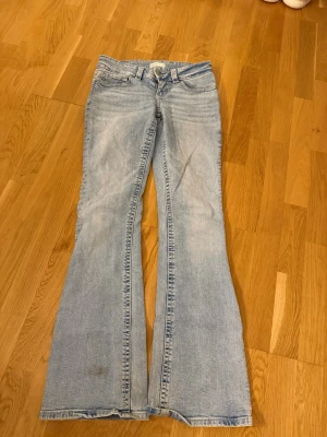 Ljusblå bootcut jeans - Säljer ett par ljusblå bootcut jeans med klassisk femficksdesign och låg midja. Jeansen har utsvängda ben och är tillverkade i mjuk denim. Perfekta för en avslappnad och trendig look.