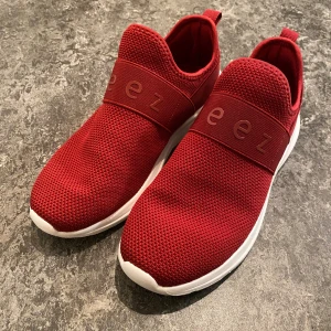 Beez Bliss Slip-on Sneaker, Vinröd - Snygga röda sneakers från Beez med vit sula och elastiskt band över foten som jag köpte från Vårdväskan. Ovandelen är i mesh-liknande syntetmaterial som andas och ger en sportig vibe. Skorna har platt, stötdämpande sula och rund tå. Perfekta arbetsskor för arbete inom tex vården och VFU. Säljer pga köpte fel storlek (för små).