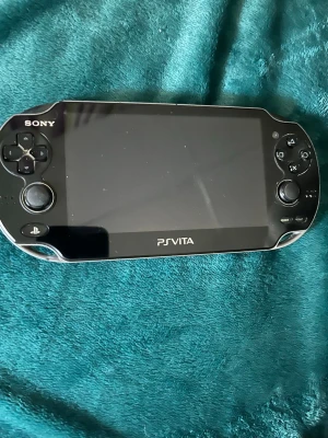 Sony PS Vita bärbar spelkonsol - Säljer en svart Sony PS Vita, en smidig och kraftfull bärbar spelkonsol med stor skärm och klassiska PlayStation-knappar. Perfekt för gaming på språng och har en snygg, modern design i plast och glas. Passar dig som vill ha portabel spelupplevelse. was working before, no charger, no box, some scratches