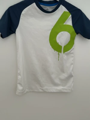 Vit och blå t-shirt med gröna detaljer. - En snygg Adidas T-shirt. Från 9-10 år och är 140 cm och inte det som står på annonsen.