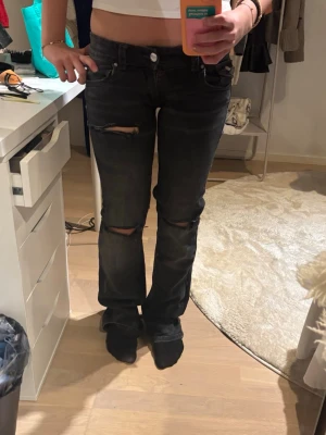 Svarta slitna jeans med raka ben - Säljer ett par svarta jeans med raka ben och slitningar vid knäna. Jeansen har klassisk femficksdesign och silverfärgade knappar på bakfickorna. Perfekta för en avslappnad och trendig look. Dem är insydda i benen. Skriv privat för mått, pris kan diskuteras