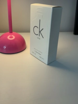 CK One Eau de Toilette 100 ml - CK One från Calvin Klein är en klassisk unisex parfym i en frostad, transparent glasflaska med silverfärgad skruvkork. Flaskan rymmer 100 ml och kommer i en stilren vit kartong med minimalistisk design och grå text. #calvinklein #parfym #ckOne