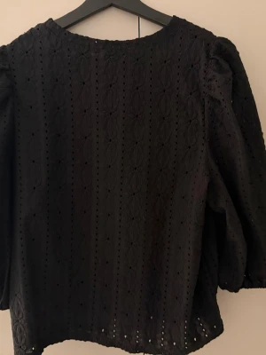 Svart blus med broderade detaljer - Säljer en svart blus med broderade detaljer och hålmönster. Blusen har rund halsringning och puffiga trekvartsärmar. Den är i storlek S från jdy