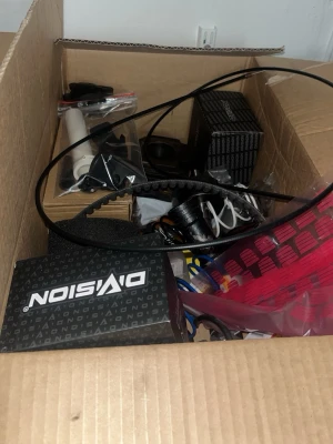 Slider delar  - Säljer en stor låda fylld med blandade bilprylar och tillbehör, bland annat från märket Dvision. Innehåller blandade delar som remmar, röda plastdetaljer, sladdar och små reservdelar. Perfekt för dig som gillar att meka eller behöver extra bildelar.