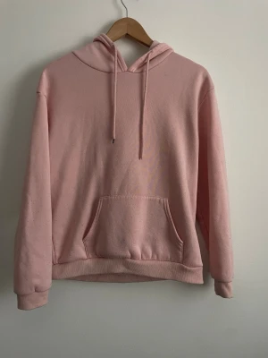Rosa hoodie med tryck bak - Säljer en ljusrosa hoodie med huva och magficka. Baksidan har ett coolt tryck med texten 'Intense Feelings' och en konstnärlig bild i svart, vitt och rosa. Perfekt för dig som gillar streetstyle och vill sticka ut lite extra.