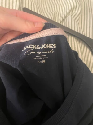 Mörkblå Jack & Jones t-shirt - Snygg mörkblå t-shirt från Jack & Jones Originals med tryck i pastellfärger på bröstet. Klassisk rund hals och korta ärmar. Tillverkad i mjuk bomull som känns skön mot huden. Perfekt för en avslappnad och trendig look.