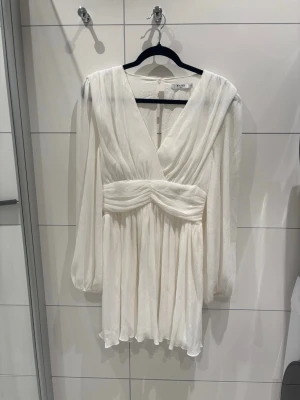 Perfekta studentklänningen - Snygg vit kortklänning med omlott framtill och markerad midja. Klänningen har långa tunna ärmar. Perfekt till studenten. Har endast använts en gång och är fläckfri och utan andra deffekter. Jag köpte denna för 649kr, den finns inte längre att köpa så vill man ha en unik klänning till student eller annat tillfälle är denna perfekt. Klänningen är i strl S, men passade perfekt för mig som skiftar mellan S och M. 