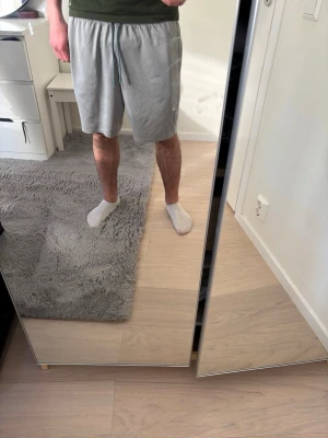 Gråa shorts med snörning - Säljer ett par gråa shorts med snörning i midjan. De har en avslappnad passform och är perfekta för varma dagar. Shortsen är tillverkade i mjukt material och har fickor på sidorna.