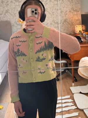 Pastellfärgad kofta från ZARA - Säljer en söt kofta från ZARA i pastellfärger med motiv av får, moln och landskap. Koftan har ljusgröna muddar och knappar, ljusrosa ärmar och kropp med grönt och vitt mönster. Det finns någon enstaka lös tråd, se bilder. Vet inte vad det är för material men koftan är varm!Rund halsringning och croppad modell. Perfekt för dig som gillar gulliga detaljer!