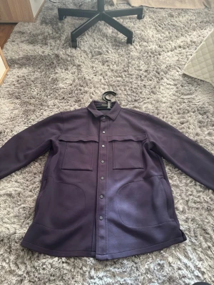 Blå overshirt med fickor - Snygg blå overshirt med klassisk krage och tryckknappar framtill. Två stora bröstfickor med lock och två sidofickor. Overshirten har en rak passform och är tillverkad i ett mjukt, lite tjockare material som ger en stilren look. Står storlek L på tröjan men passar M mycket bättre.