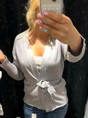 Ljusgrå kofta med omlottkofta knytband - Snygg ljusgrå kofta. Den är väldigt mjuk och har följsam passform, perfekt att slänga över ett linne eller t-shirt. Enkel och stilren design som passar till jeans eller kjol.