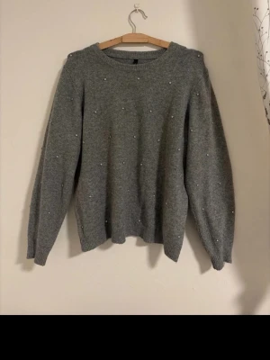 Grå stickad tröja med pärlor - Mysig grå stickad tröja med små pärlor över hela fram- och baksidan. Tröjan har rund halsringning, långa ärmar och ribbade muddar vid ärmslut och nederkant. 