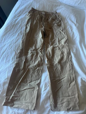 Beiga byxor med resårmidja - Snygga beiga byxor med avslappnad passform och resår i midjan. Byxorna har raka ben och dragsko i midjan för extra komfort. Perfekta för en chill och stilren look. Materialet är luftigt som passar bra till varmare dagar. Behöver strykas 