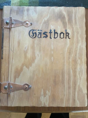 Rustik gästbok i trä med metallbeslag - Säljer en unik gästbok med omslag i ljust trä och snygga metallbeslag. Texten 'Gästbok' är ingraverad på framsidan i gammaldags stil. Perfekt för bröllop, fester eller som minnesbok. Inlagan består av blanka vita sidor redo att fyllas.Gsmmsl antik i nyskick 