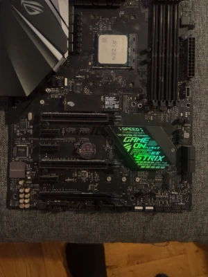 ASUS ROG Strix moderkort med Ryzen CPU - Säljer ett ASUS ROG Strix moderkort med AMD Ryzen-processor installerad. Moderkortet har svart design med RGB-detaljer, flera RAM-platser, PCIe-portar och många anslutningar som USB, HDMI och ljudutgångar. Perfekt för gamingbygge eller uppgradering.