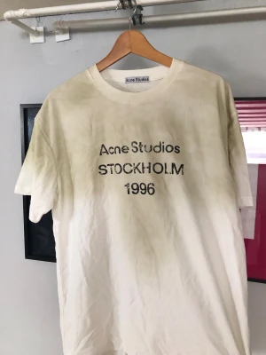 Vit Acne Studios t-shirt - Vit t-shirt från Acne Studios med svart texttryck 'STOCKHOLM 1996' på bröstet. Klassisk rund hals och korta ärmar. Köpt av någon annan här på Plick, därav inte mina bilder. Säljer vidare då jag inte är nöjd med passform 💕