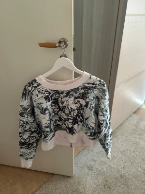 Vit och svart mönstrad hoodie - Säljer en kort hoodie med unikt svartvitt marmormönster och dragkedja backtill. Tröjan har långa ärmar, ribbade muddar och en bred, vit kant vid hals, ärmslut och nederkant🤍🤍