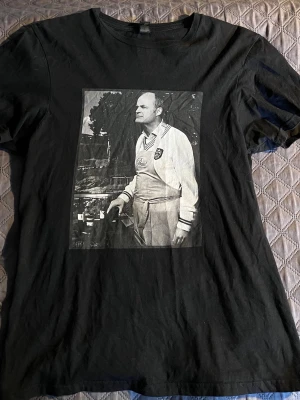 Svart t-shirt med Fredrik Schiller tryck - Cool svart t-shirt med ett stort svartvitt fototryck på framsidan som ger en retrovibe. T-shirten har rund hals och korta ärmar, perfekt för en avslappnad stil. Materialet känns mjukt och bekvämt mot huden.