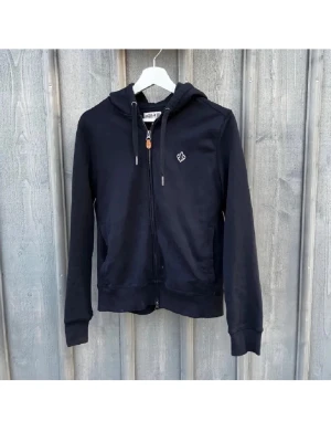 MORRIS HOODIE ZIP - Svart Morris zip hoodie med dragkedja framtill och huva med snören. Liten vit broderad logga på bröstet och ribbade muddar vid ärmar och nederkant. Tillverkad i mjukt material, perfekt för en avslappnad stil.