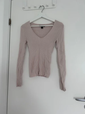 Beige ribbad tröja med v-ringning - Supersnygg ljusrosa ribbad tröja med djup v-ringning och långa ärmar. Tröjan är figurnära och har en mjuk, stretchig känsla som passar perfekt till jeans eller kjol. Enkel men trendig design som är lätt att matcha.