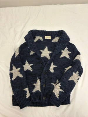 Ralph Lauren Denim and Supply kofta - Säljer en chunky mörkblå stickad kofta från Ralph Lauren x Denim Supply . Koftan har bred krage, knappar framtill och ribbade muddar vid ärmslut och nederkant. Perfekt för dig som gillar statement-plagg och mysig stil.