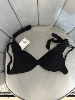 Svart bikini-bh med knytband - Snygg svart bikini-bh med knytband i nacken och ryggen. Bh:n har släta kupor utan vaddering och ger en enkel och stilren look. Perfekt för strand eller poolhäng och lätt att matcha med olika underdelar.