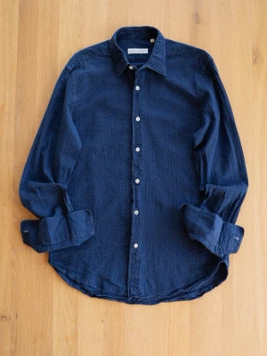 Blå seersucker från Nitty Gritty, size S - Säljer en mörkblå skjorta från Nitty Gritty i bomull med strukturerad yta. Skjortan har klassisk krage, långa ärmar och vita knappar framtill. Perfekt för dig som gillar stilrena och bekväma plagg.