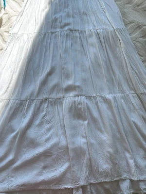 Vit långkjol - Jag säljer en vit basic långkjol från lager 157. Den är perfekt nu till sommaren eftersom den är tunn och avslappnad. Perfekt för en somrig look. Kjolen har däremot en lite fläck på framsidan som man ser på bild 2. Den är ej jätte synlig dock. Står att kjolen är en storlek L men passar utmärkt som en S/XS