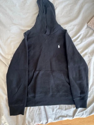 Svart hoodie från Polo Ralph Lauren - Säljer en svart hoodie från Polo Ralph Lauren med klassisk vit broderad logga på bröstet. Storlek L barn (14-16 år). Knappt använd.