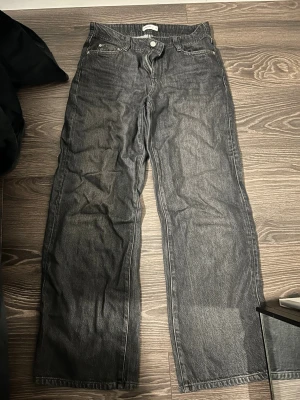 Svarta raka jeans från Ginatricot  - Säljer ett par svarta raka jeans från Ginatricot i storlek 36. Jeansen har klassisk femficksmodell, silverfärgade knappar och kontrastsömmar. Materialet är denim med en något lös passform och lågmidja.
