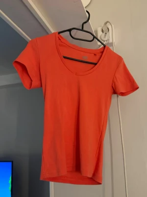  t-shirt med v-ringning - En enkel och snygg korallröd t-shirt med v-ringad hals och korta ärmar. Perfekt till jeans eller shorts för en avslappnad look.