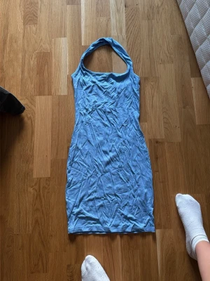 Ljusblå ärmlös kortklänning - Säljer en ljusblå, tight och ärmlös kortklänning med halterneck. Klänningen har en enkel och stilren design, perfekt för dig som gillar en clean look. Materialet känns mjukt och stretchigt, vilket gör den bekväm att bära.