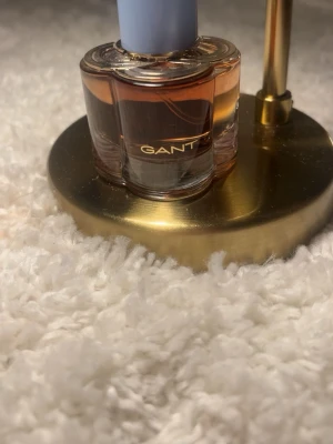 GANT Eau de Parfum 30 ml - Säljer en elegant parfym från GANT i en unik fyrklöverformad glasflaska med ljusblått lock. Flaskan har en varm bärnstensfärgad vätska och guldtext på framsidan. Perfekt för dig som gillar stilrena och klassiska dofter. Detta är gant sunset club!
