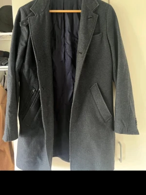 Mörkblå klassisk ullrock - Säljer en mörkblå herrkappa i klassisk modell. Perfekt för höst och vinter, både till vardags och mer uppklädda tillfällen. Kappan har en tidlös design med slagkrage, sidofickor och mörkt innerfoder. 	•	Färg: Mörkblå 	•	Modell: Knälång herrkappa 	•	Skick: Bra begagnat skick 	•	Passar både jeans och kostym  Säljes eftersom den inte längre används. Någon skavank i ena armhålan, men inget som syns utvändigt.