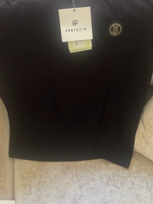 Svart t-shirt med rund hals - Snygg svart t-shirt med rund hals och diskret logga på bröstet. T-shirten har korta ärmar och är tillverkad i mjuk bomull, perfekt för en clean och stilren look.