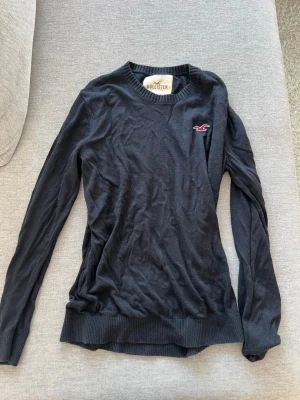 Mörkblå tröja från Hollister -  långärmad tröja från Hollister med rund halsringning och ribbade muddar. Tröjan har en liten röd logga broderad på bröstet. Perfekt för dig som gillar enkel och stilren design.