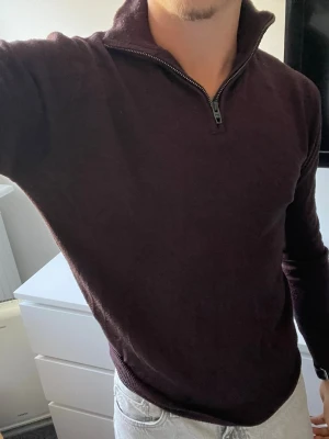 Mörklila halvzip tröja - Snygg mörklila tröja med halvzip och hög krage. Tröjan har lång ärm och är i en mjuk, stickad kvalitet. Perfekt för dig som gillar stilrena och bekväma plagg med en modern touch.