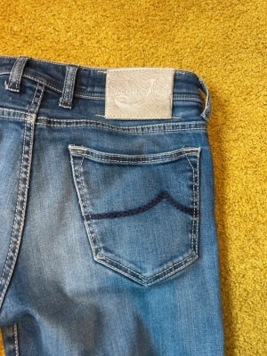 Blå jeans från Jacob Cohen - Snygga blå jeans från Jacob Cohen med klassisk femficksmodell och raka ben. Jeansen har en ljus tvätt och kontrastsömmar samt en dekorativ detalj på bakfickan. Tillverkade i mjuk denim för skön passform.