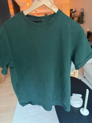 Mörkgrön loose fit t-shirt från H&M - En stilren mörkgrön t-shirt från H&M i loose fit-modell. T-shirten har rund halsringning och korta ärmar. Perfekt för en avslappnad och trendig look. Tillverkad i mjuk bomull för extra komfort.