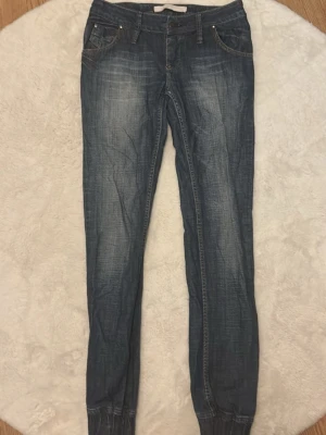 Blå jeans med resår vid benslut - Snygga blå jeans med tvättade detaljer och resår vid bensluten. Klassisk femficksmodell med dragkedja och knapp framtill. Jeansen har smal passform och kontrastsömmar för en cool look.