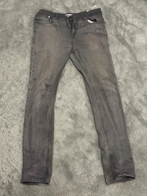 Grå Tommy Jeans - Säljer ett par gråa skinny jeans från Tommy Jeans med klassisk femficksdesign och knappgylf. Jeansen har en tvättad look och smal passform som sitter snyggt längs benen. Perfekta för en avslappnad och trendig stil.