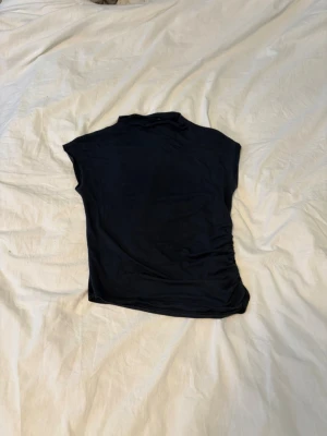 Topp med hög hals - Mörkblå, nästan svart topp med hög hals och korta ärmar från lager 157. Toppen har en lätt rynkad detalj på ena sidan vilket ger en snygg twist. 