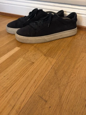 Svarta sneakers från Marc O'Polo - Stilrena svarta sneakers från Marc O'Polo med ovandel i mocka och klassisk vit sula. Lågt skaft och snörning framtill ger en clean look som passar till det mesta. Perfekta för dig som gillar enkel och tidlös stil.