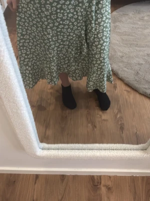 Grön blommig långkjol med volang - Säljer en grön långkjol med vitt blommönster och volangkant nedtill. Kjolen har en avslappnad passform och är perfekt för dig som gillar en feminin och trendig stil. Materialet känns lätt och flowy, perfekt för varmare dagar.