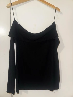 Svart offshoulder ribbad topp - Svart offshoulder topp med ribbad struktur och långa ärmar. Perfekt för dig som vill ha en stilren och snygg look. Snyggt fall över axlarna.