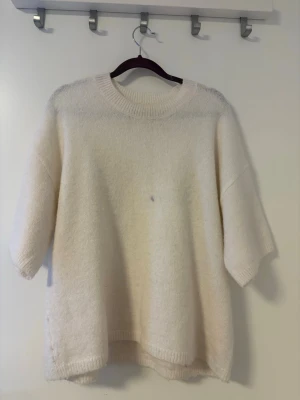 Oversized vit stickad tröja - Mysig oversized stickad tröja i offwhite med rund halsringning och halvlånga ärmar. Tröjan har en avslappnad passform och ribbstickade detaljer vid hals, ärmslut och nederkant. 
