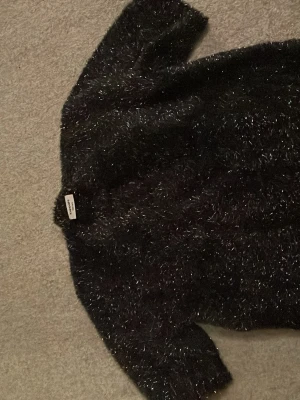 Svart teddy kofta  från Kappahl - Säljer en svart teddy kofta från Kappahl i storlek 158/164. Koftan har fluffigt, glansigt material med inslag av silvertrådar som ger en cool och trendig look och ser ut som en glittrig skön look. Perfekt för dig som vill ha en mysig,snygg och glittrig kofta till hösten eller vintern. Nypris 300kr. Mitt pris 80kr men kan diskuteras!🫰🏻