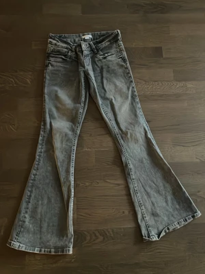 Grå bootcut jeans med låg midja - Säljer ett par grå bootcut jeans med låg midja och klassisk femficksmodell. Jeansen har en tvättad look och vida ben som ger en retro vibe. Perfekta för dig som gillar en avslappnad men ändå trendig stil.