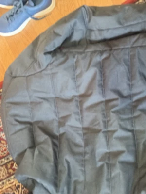 Svart quiltad jacka med dragkedjor - Snygg mörkgrå quiltad jacka med ståkrage och dragkedja framtill. Jackan har tre fickor med svarta dragkedjor och en knappdetalj vid halsen. Perfekt för kyligare dagar och ger en stilren look.